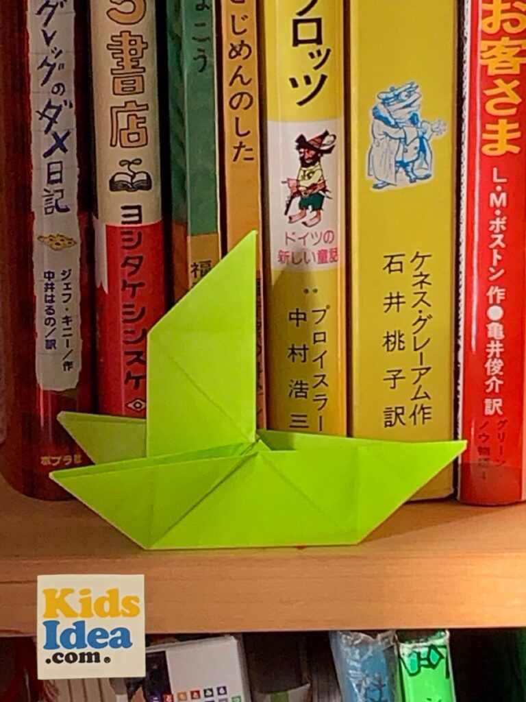 Origami ship placed in front of the book on the bookshelf ©︎2023 kids-idea.com