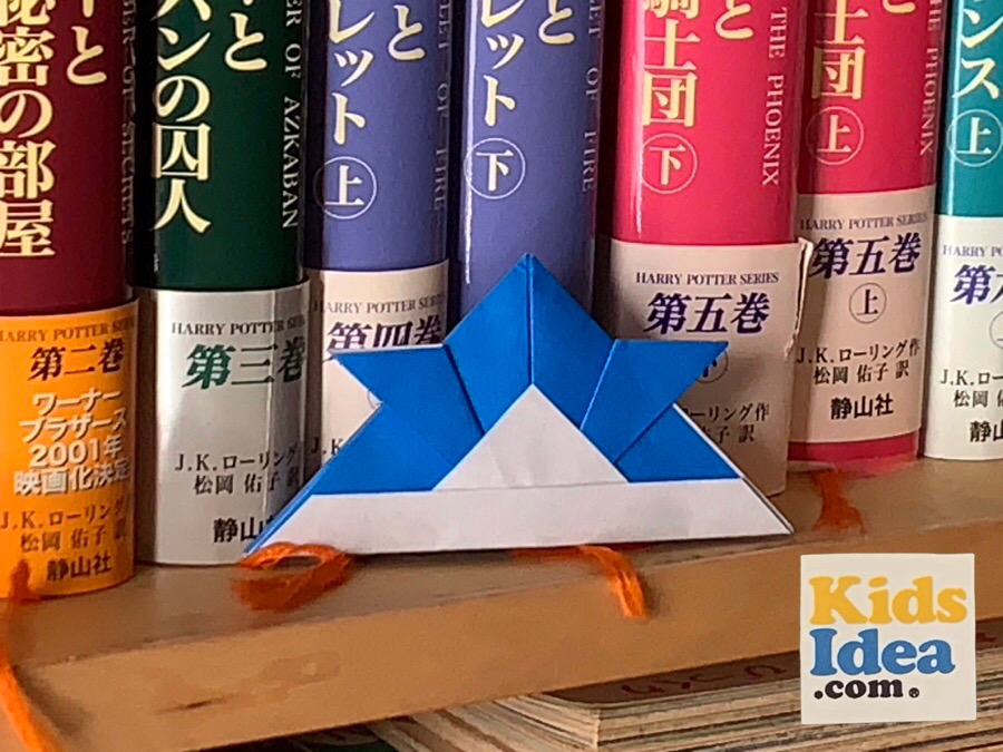 Origami "helmet" placed in front of a book on the bookshelf ©︎2023 kids-idea.com